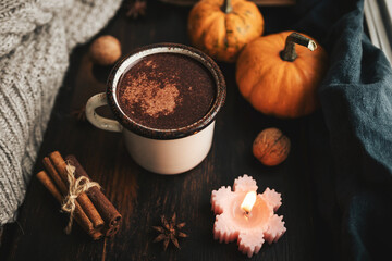 Cozy autumn scene with mug of hot chocolate, pumpkins, spices and candles on rustic dark wooden...