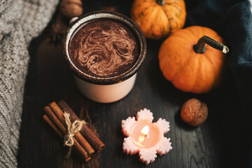 Cozy autumn scene with mug of hot chocolate, pumpkins, spices and candles on rustic dark wooden background, warm seasonal atmosphere