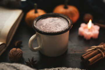 Cozy autumn scene with mug of hot chocolate, book, pumpkins, spices and candles on rustic dark wooden background, warm seasonal atmosphere