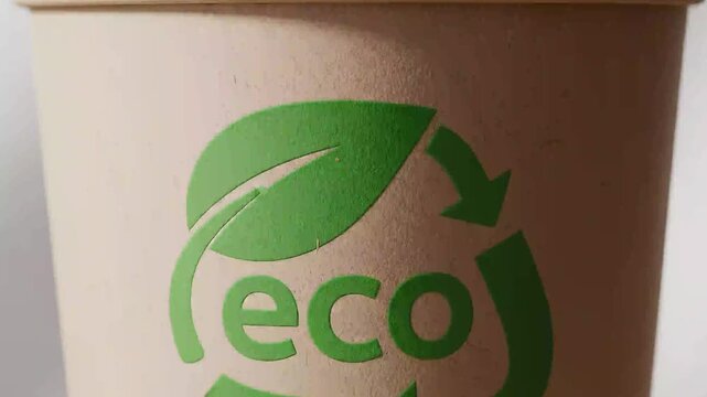 Close up of paper coffee cup with green eco recycling symbol, environmental consciousness and sustainable living, environmental protection concept