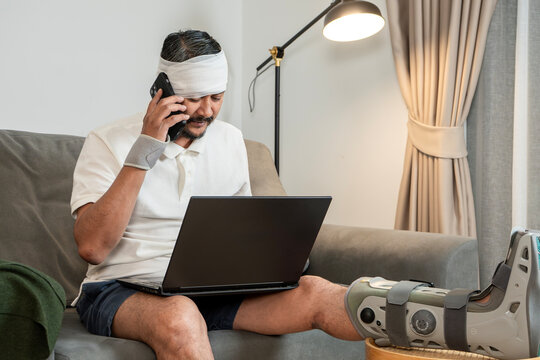 A young man with a leg cast and head bandage works from home, concept of accident insurance and income compensation.