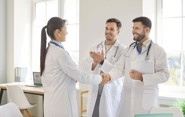 Happy doctor hand shake to admire and agree with medical diverse staff in hospital, welcoming new colleagues, practitioners in white uniforms, standing in office hall, discussing teamwork, applauding