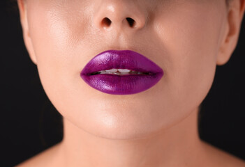 Fototapeta premium Woman with beautiful purple lipstick on her lips against black background, macro view