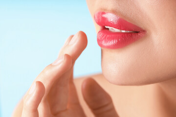 Woman with beautiful pink lipstick on her lips against light blue background, macro view