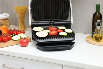 Electric grill with vegetables on white countertop in kitchen