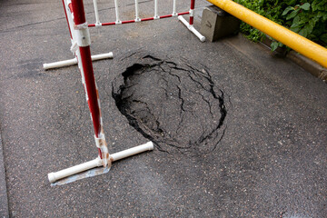 Hole in the road with a red and white fence in the background
