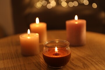 Burning candles on wooden table against blurred lights, closeup