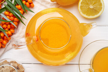 Sea buckthorn tea, fresh berries, sugar cubes and lemons on white wooden table, flat lay