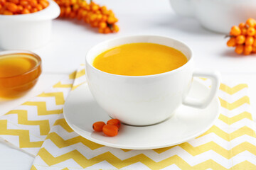 Sea buckthorn tea in cup, honey and fresh berries on white table, closeup