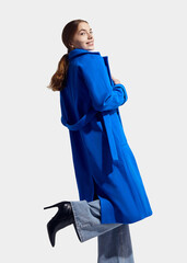 a beautiful woman in a long blue coat on a light background