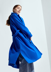 a beautiful woman in a long blue coat on a light background