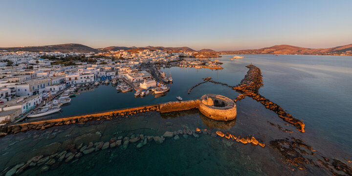 Aerial view of whitewashed buildings meet the azure sea, a stone fortress standing guard as boats bob gently in the harbor, Paros, Paros, Greece.