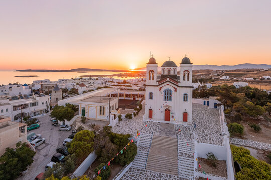 Aerial view of whitewashed buildings and a church with red doors bask in the warm glow of the setting sun, Paros, Paros, Greece.