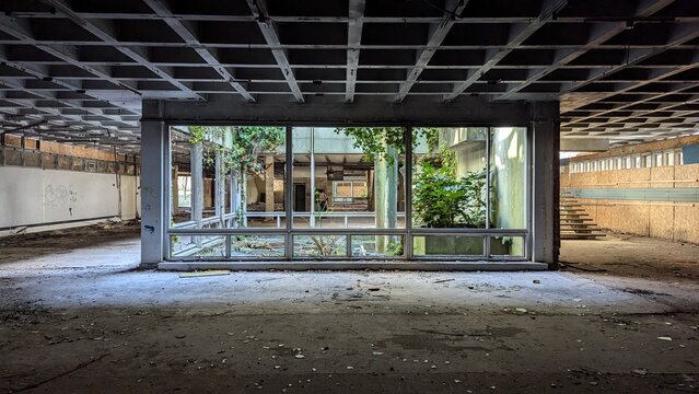 Abandoned industrial atrium terrarium, interior garden inside derelict ruins. Eerie natural light space, concrete grid ceiling, indoor plants, deserted crumbling architecture. Empty post apocalyptic.