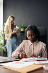 Obraz premium Black businesswoman writing notes while colleague works in office