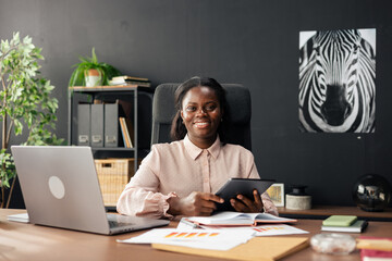 Black businesswoman smiling working at desk holding tablet