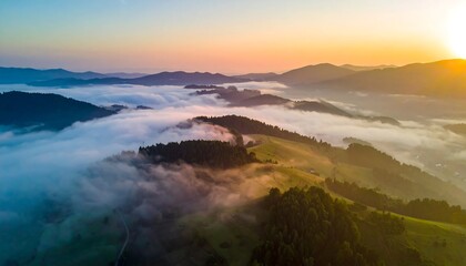 An aerial view displays a vibrant sunrise over a mountain range, thick fog nestled in valleys, creating a serene natural scene. The sun's glow bathes the landscape