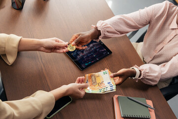 Women exchanging bitcoin for euro banknotes on desk