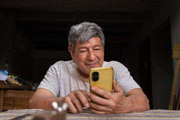 An elderly Colombian man is happy while chatting with distant family via smartphone inside his home in Neiva, Huila, Colombia. concept of technology and aging
