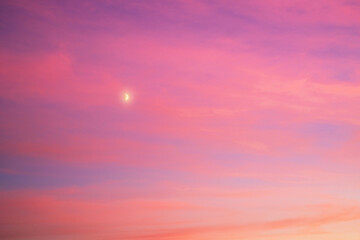 A crescent moon in a vibrant colorful evening sky with pink and purple clouds at sunset. Atmospheric twilight scene