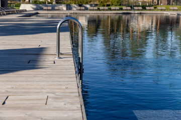 A Tranquil Reflection of Nature: A Close-Up View of a Modern Poolside with a Sleek Metal Ladder and Calm Waters Under a Clear Sunny Sky