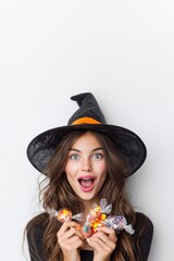 Portrait of a joyful surprised woman wearing witch costume holing candies for Halloween celebration.