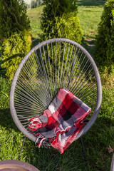 An Inviting Outdoor Space with a Stylish Black Woven Chair and a Cozy Red and Gray Blanket Resting Comfortably Over Its Arm in a Green Setting