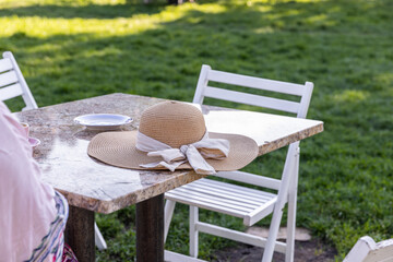 A Relaxing Outdoor Scene Featuring a Stylish Straw Hat on a Table Surrounded by Greenery, Perfect for a Summertime Afternoon Tea Experience