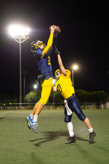 Naklejka premium American football players jumping catching ball during night game
