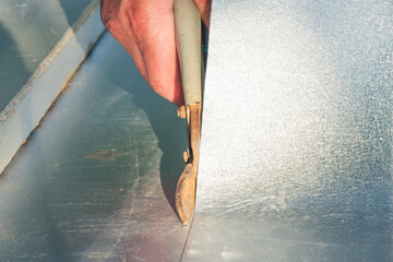 A worker cuts a sheet of tin with metal shears