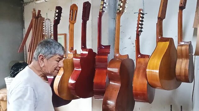 Portrait of an elderly Latino man playing several acoustic guitars hanging from a pole inside a luthier workshop in Neiva, Huila, Colombia. Concept of lifestyle active 