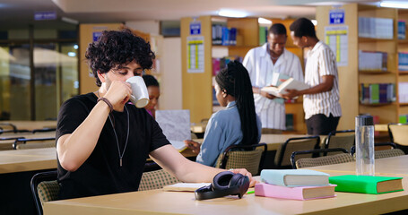 Indian young adult gen z busy male man sitting on chair read book indoor library campus place. Teen...