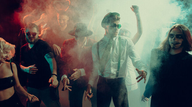 Group of friends in Halloween costumes dancing in nightclub with smoke and neon lights. Concept of entertainment, party advertising, music industry and youth lifestyle.