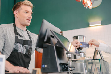 close-up image focuses on a barista and a customer during a payment transaction at a counter.