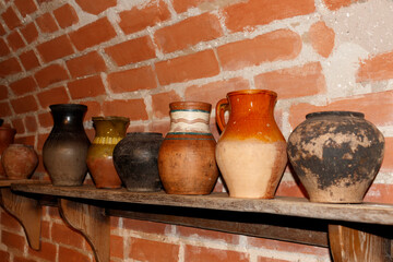 Set of clay pot and ceramic kitchenware which is kept on the wooden shelf in red brick wall storage room. Interior object photo.