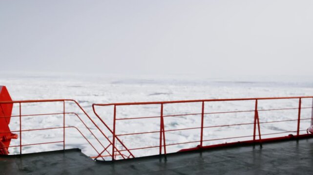 Polar ship deck with orange railing overlooking a field of drifting sea ice fading into a misty horizon, evoking winter passage and careful navigation through frozen waters.
