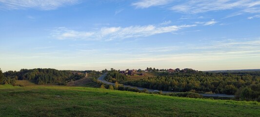 Picturesque view of rural landscape with winding road, green fields, and cluster of houses nestled...
