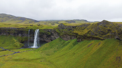 Majestic waterfall flows down rocky cliffs into a serene pool, surrounded by vibrant green hills and valleys, creating a peaceful atmosphere that highlights the beauty of nature and its tranquility