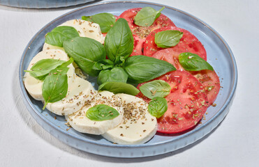 Classic Caprese salad with sliced ​​fresh tomatoes, mozzarella and basil leaves on a blue plate
