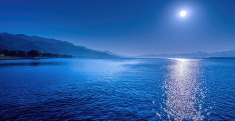 Fototapeta premium Serene nightscape depicts a shimmering lake reflecting the full moon and distant mountain range