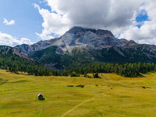 Beautiful landscape in Dolomites, Italy.  Malga Prato Piazza meadow and big mountain summit and ridge. South Tyrol region in Italy. Trekking and bike road in Italy Dolomites. Wooden cabin hut.
