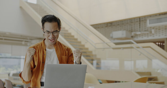 Senior Asian businessman wearing headset celebrates success during online meeting in modern co-working space. Remote work and business communication concept	