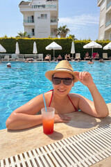 Smiling woman in hat relaxing in hotel swimming pool