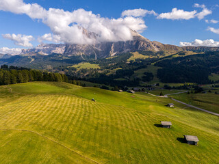 Aerial view over meadows in front of Alpe di Siusi peaks, in Dolomites, Italy. Beautiful hut on alpine plateau Seiser Alm. Wooden cabins in south Tyrol. Dolomites UNESCO World Heritage.
