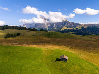 Aerial view over meadows in front of Alpe di Siusi peaks, in Dolomites, Italy. Beautiful hut on alpine plateau Seiser Alm. Wooden cabins in south Tyrol. Dolomites UNESCO World Heritage.