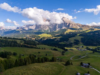 Aerial view over meadows in front of Alpe di Siusi peaks, in Dolomites, Italy. Beautiful hut on alpine plateau Seiser Alm. Wooden cabins in south Tyrol. Dolomites UNESCO World Heritage.
