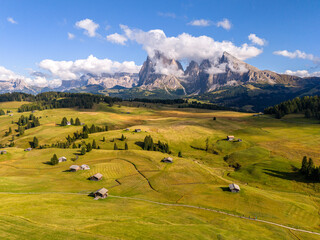 Aerial view over meadows in front of Alpe di Siusi peaks, in Dolomites, Italy. Beautiful hut on alpine plateau Seiser Alm. Wooden cabins in south Tyrol. Dolomites UNESCO World Heritage.