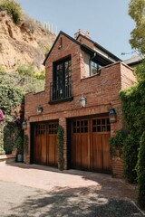 Naklejka premium Beautiful brick house with wooden garage doors situated in a scenic hillside location surrounded by vibrant greenery during a sunny day