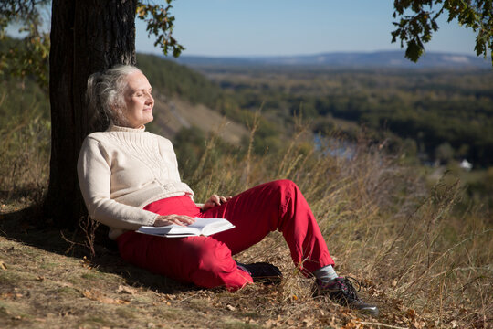  Slow life. Enjoying the little things.  lifestyle portrait senior woman  with gray hair rests and reads a book Sitting under a tree on a mountain on a sunny autumn day. 