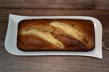 Sliced banana bread rests on a white plate, showing its rich brown color and golden crust. The sweet aroma fills the air, inviting everyone to enjoy this delicious treat.